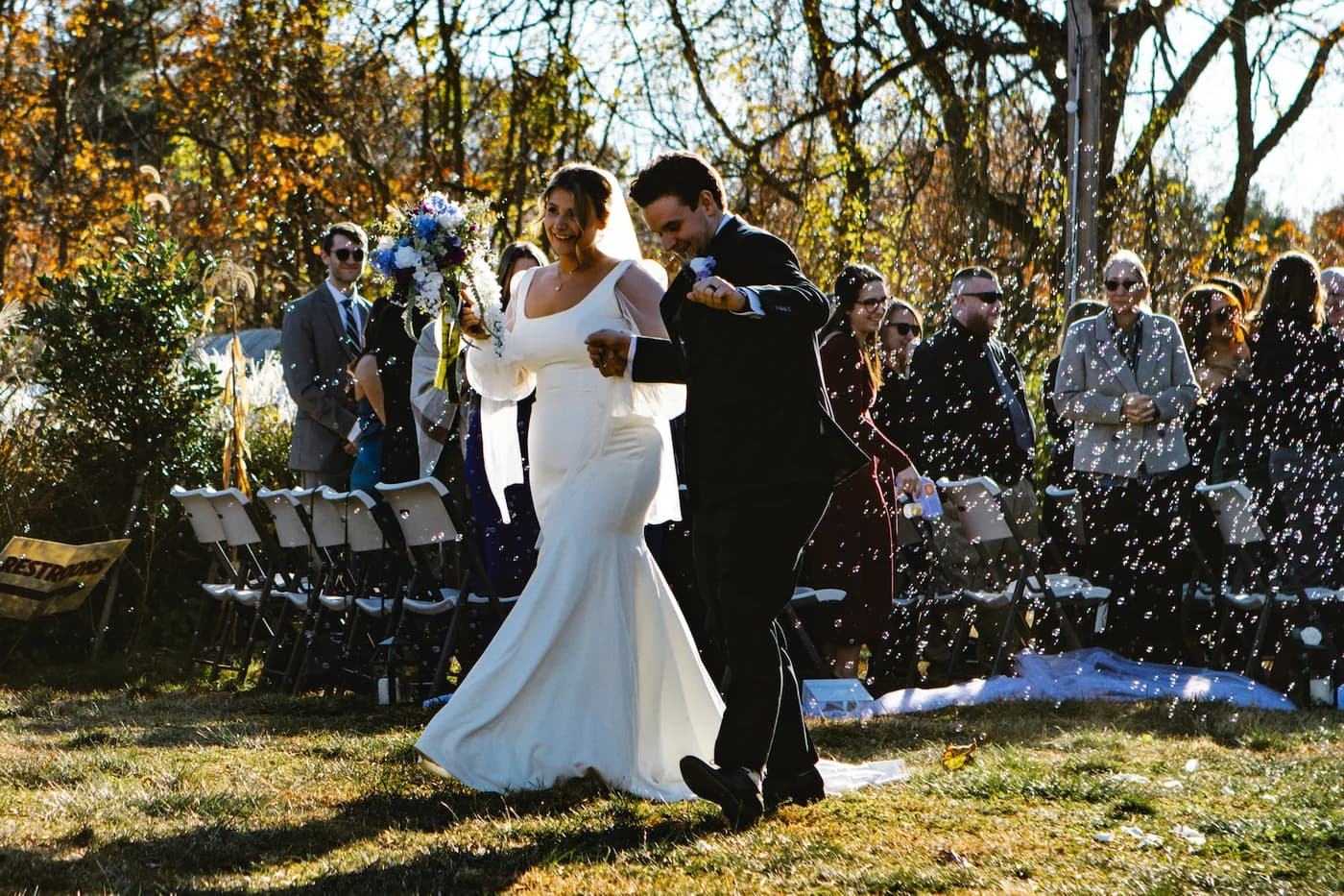 A bride and groom walking back up the aisle through bubbles at an outdoor ceremony