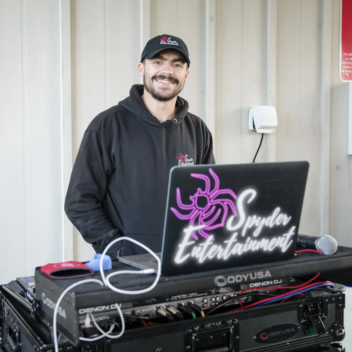 Kyle Bianco behind his DJ booth, the lit Spyder Entertainment spider on the booth facade